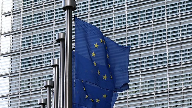 L'immagine mostra una fila di bandiere europee con parte del palazzo Barlaymont in secondo piano.