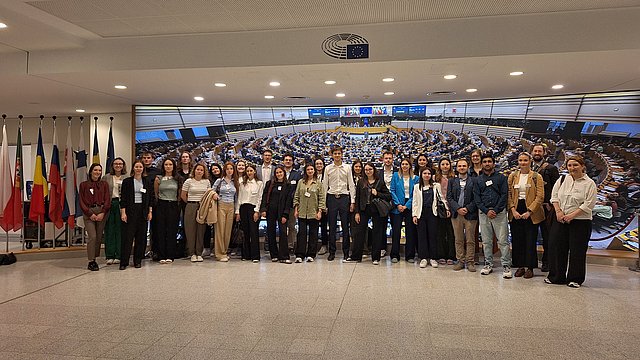 © Euregio Das Bild zeigt eine Gruppe von Jungen und Mädchen, die vor dem Plenarsaal des Europäischen Parlaments in Brüssel und den Flaggen für ein Foto posieren.