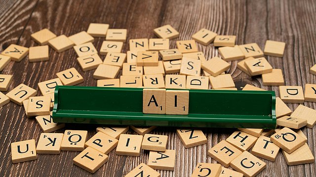 Auf einem Scrabble-Spielbrett erscheinen die Buchstaben A und I. Alle anderen Spielsteine sind auf dem Tisch verstreut. 