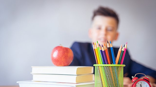 Symbolbild: Kind mit Büchern, Schreibutensilien und Apfel