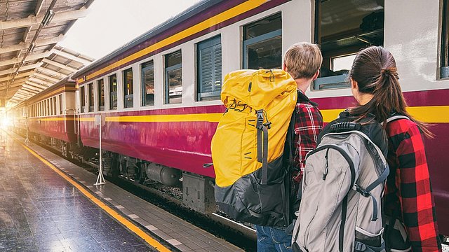 © Pexels/Veerasak Piyawatanakul Ein Junge und ein Mädchen stehen mit dem Rücken zur Kamera auf dem Bahnsteig vor einem roten Zug